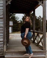 woman in black t-shirt and blue denim jeans holding brown hat